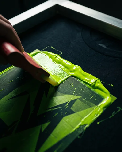 Squeegee pulling lime ink through a screen onto a black tee
