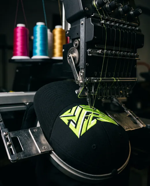 Embroidery machine stitching a lime emblem onto a black cap
